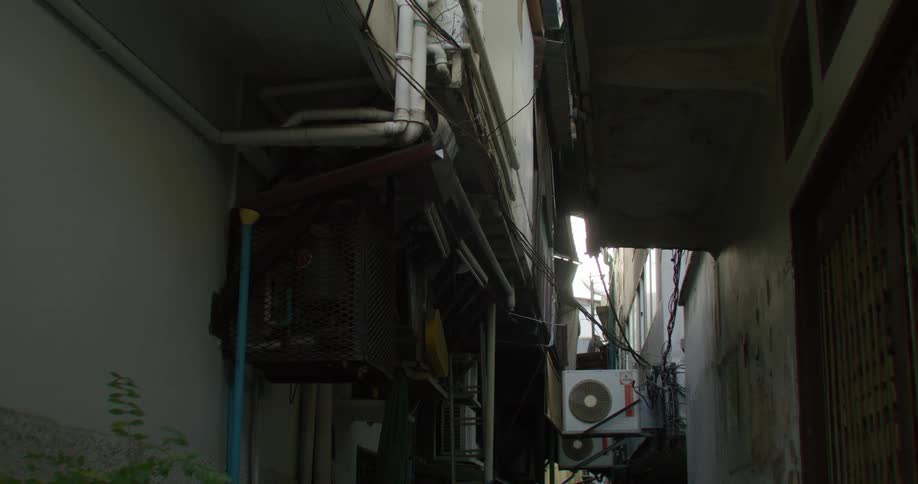 Air conditioning units stick out of buildings into a narrow alleyway between buildings during the day