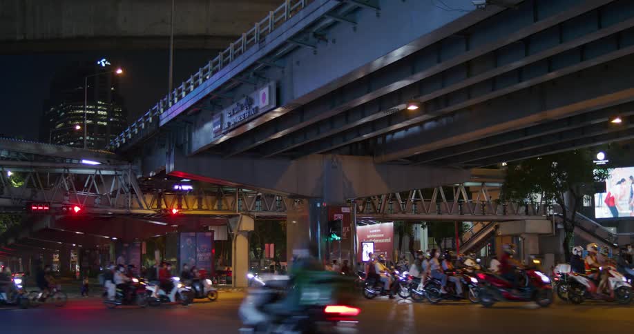 A large group of scooter riders and motorcyclists ride under an overpass downtown