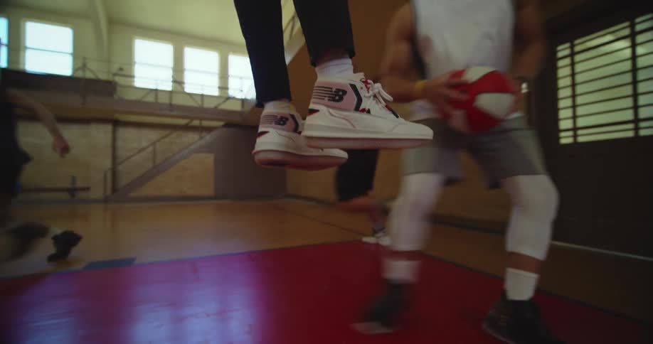 Young person hanging from the hoop in the middle of a basketball game drops down