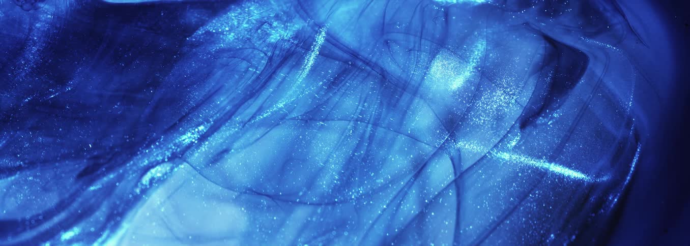 Waves of an electric blue substance move across a glittery light blue liquid area