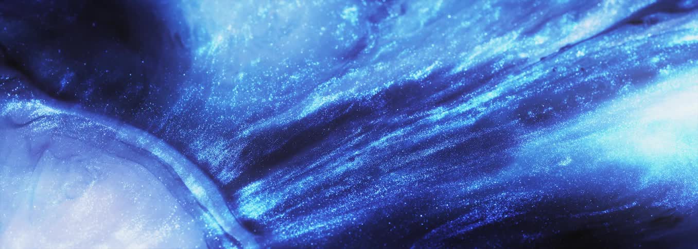 Glitter sparkles in an electric blue substance as waves of a light blue and white ripple and move across the surface