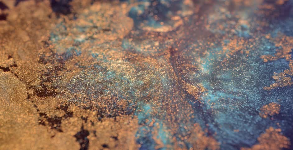 A glitter gold substance ripples and moves over a blue textured liquid