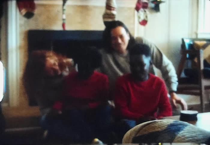 A family is sitting in front of a christmas decorated fireplace for a portrait