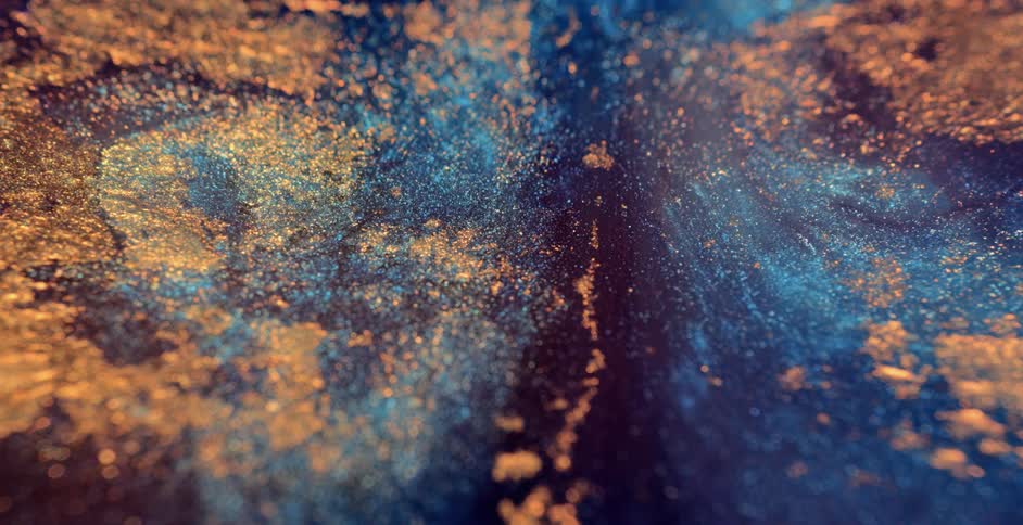 Golden particles float on surface of blue mass as it flows and spreads