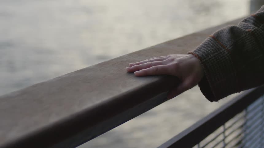 Person wearing coat runs their hand along wooden top offence on waterfront