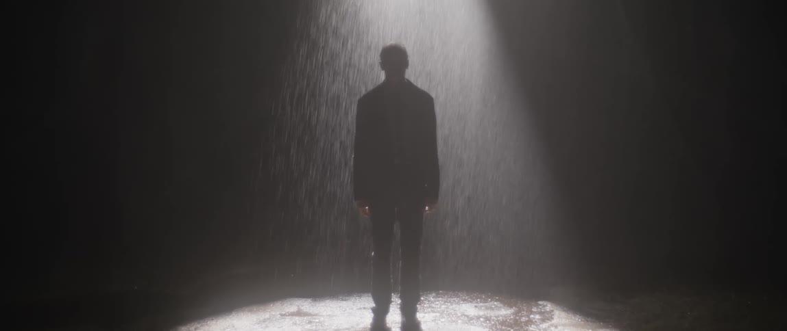 A man is standing under a light in the pouring rain at night