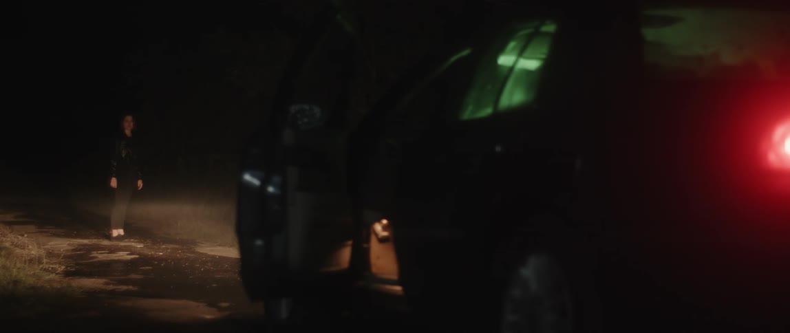 A view of a woman standing outdoors near a car