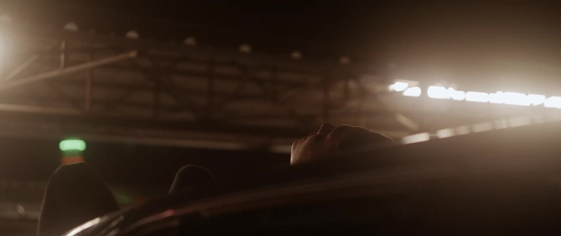 Woman laying over the hood of a car parked under neon lights at night