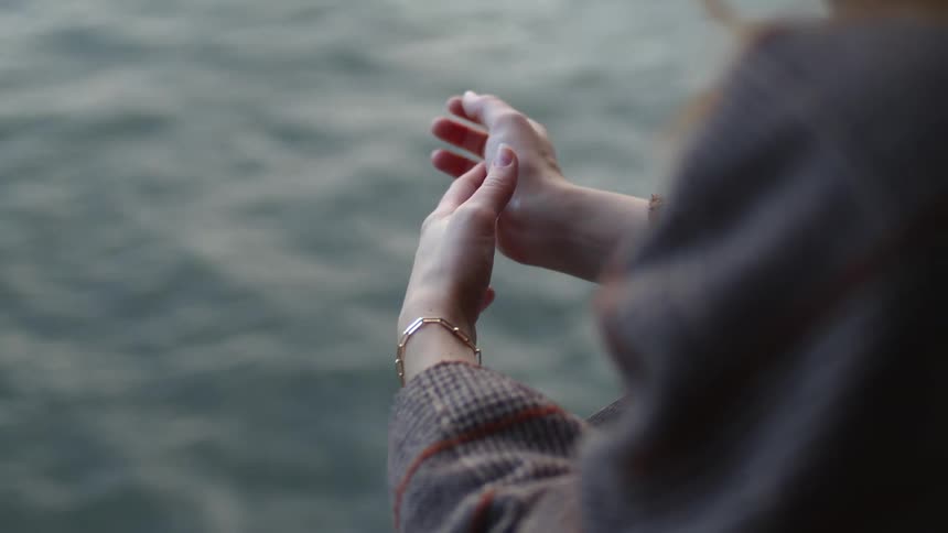 A woman rubs her hands together by the water