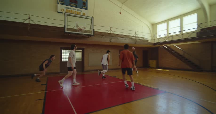 Men play basketball together in gym