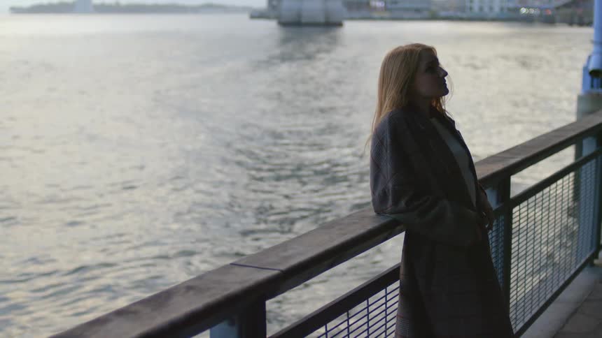 Young woman reclined on a railing next to the ocean near a coastal city