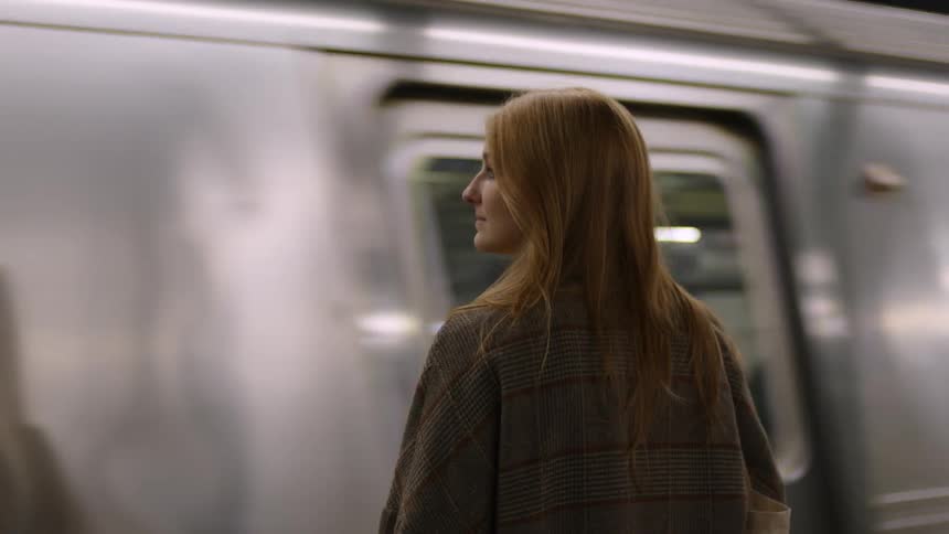 A woman stands waiting as a subway train moves in front of her