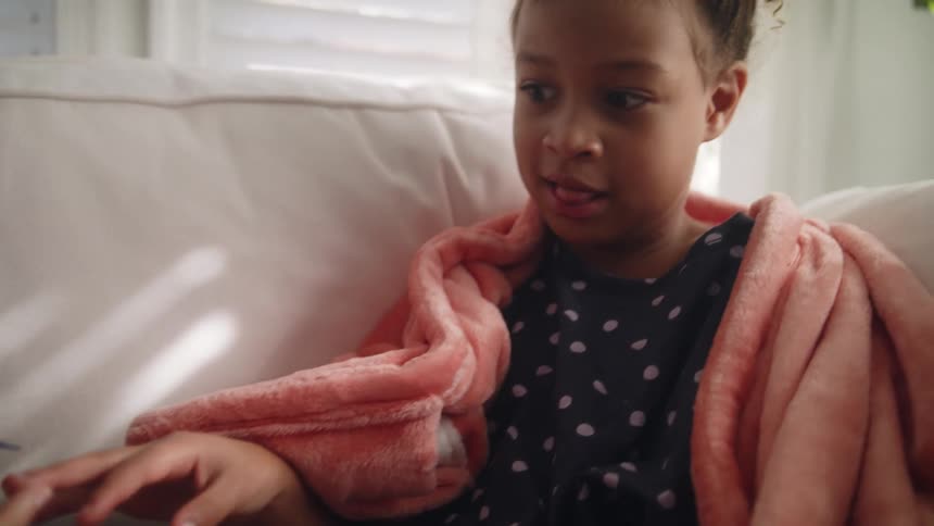 Mother paints nails of daughter as they sit on couch with blankets
