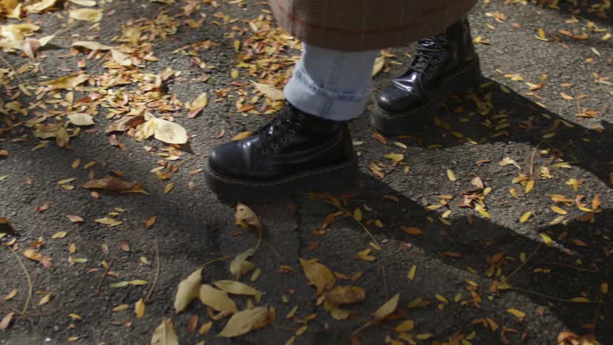 Close up of a person wearing boots walking over gravell and dead leaves