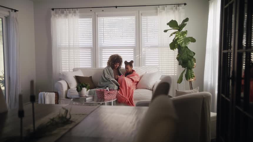 Mother gives daughter a manicure as they sit bundled in blankets on couch