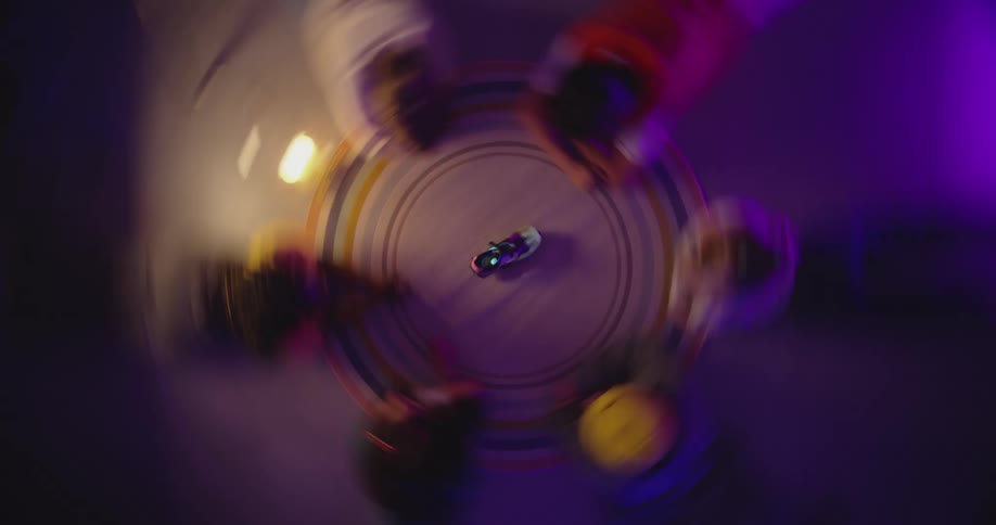 A small group of people are sitting at a round table in a dimly lit room playing spin the bottle but with a shoe