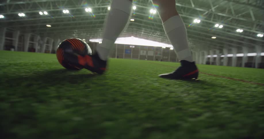 Female soccer player kicks a ball while walking on a field in a stadium