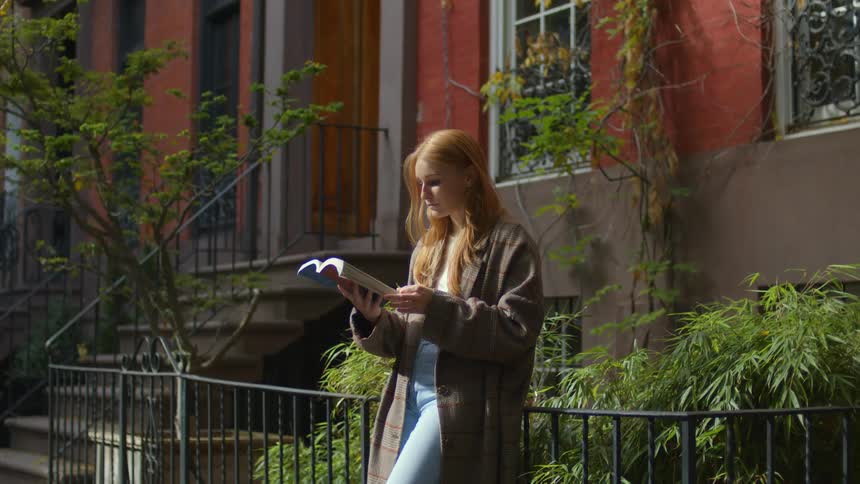 A woman is reading a book outside of her home