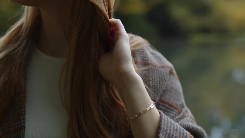 A woman is standing outside and runs her fingers through her hair