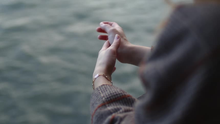 A woman is overlooking water as it ripples and moves and rubbing her hands together