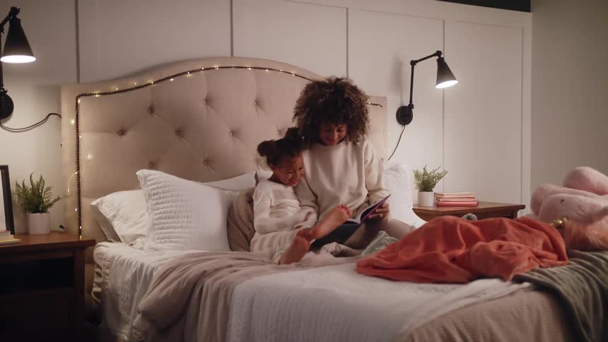 Two kids are sitting on the bed and reading a book to each other