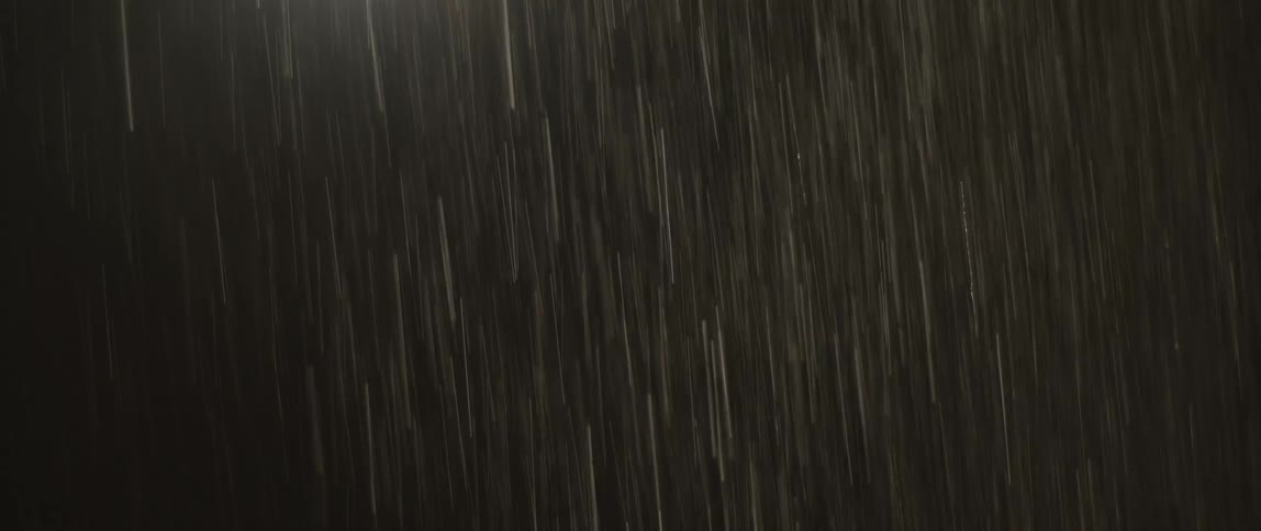 Heavy rain falls down against a dark background