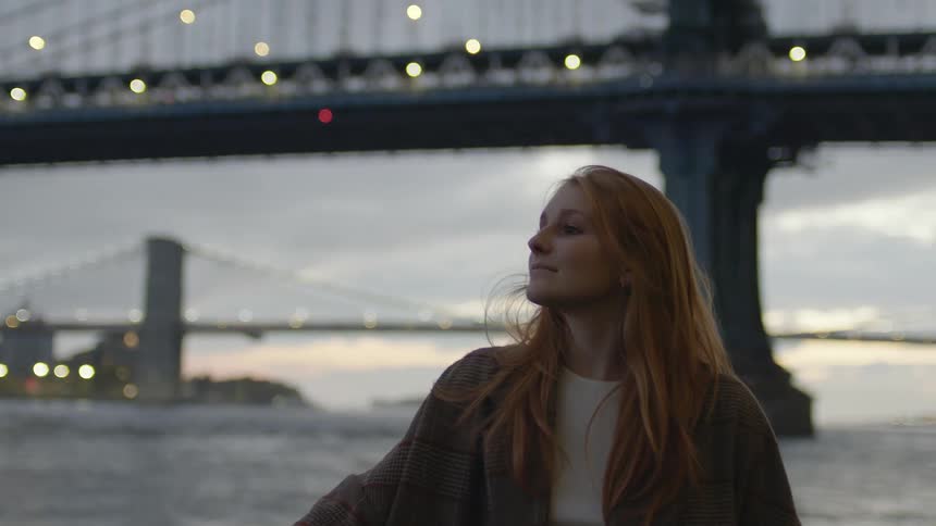 A red haired female standing near a bridge sightseeing