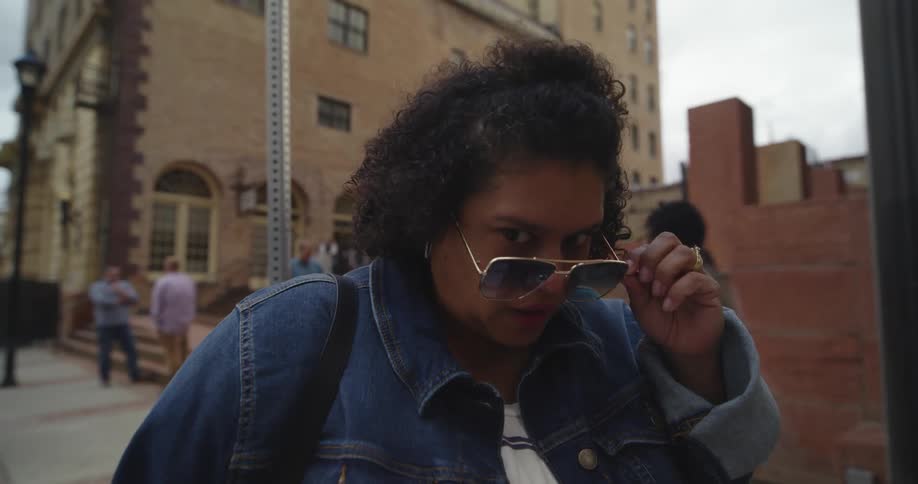 A camera goes close up to a woman looking suspicious as she pulls down her shades to look at the ground