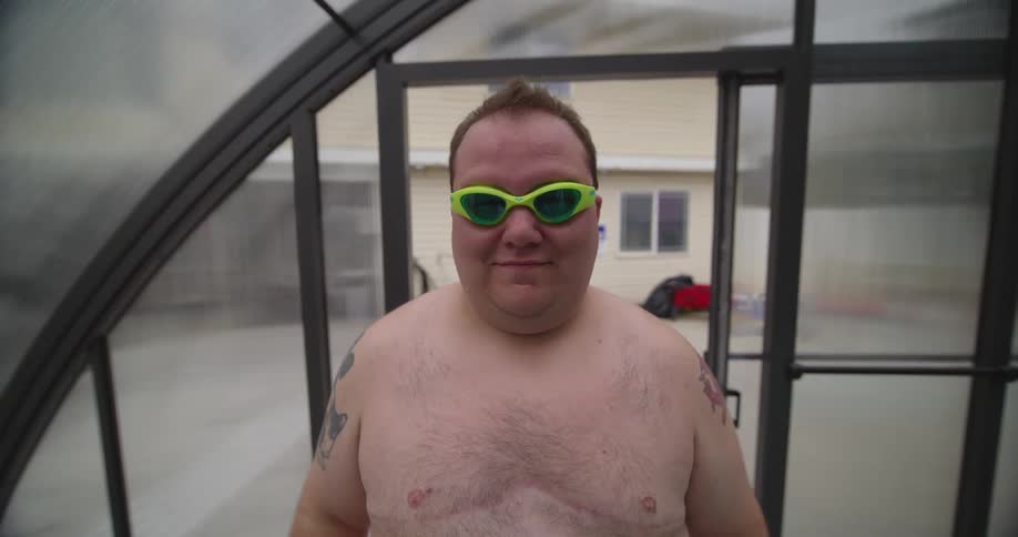 Young obese shirtless man puts on goggles before entering the pool