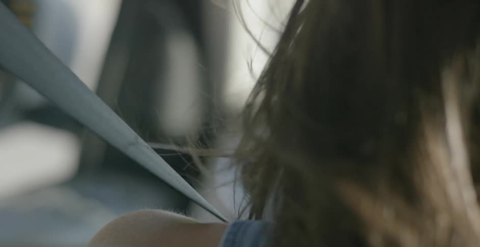A woman's hair blows in the wind while she drives with the window open in the day time