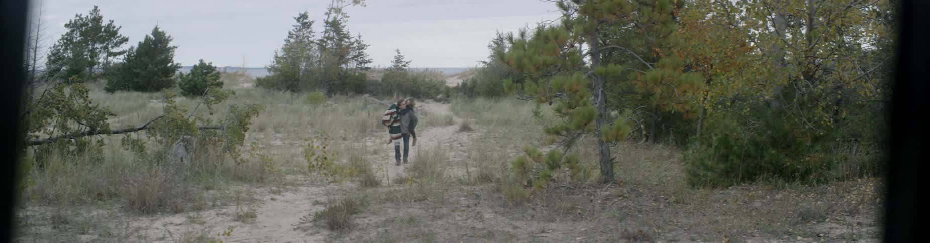 A man carries a woman on his back while walking on a path near the forest