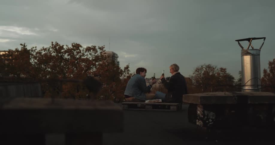 A man and woman drink beer from bottles while sitting in the park