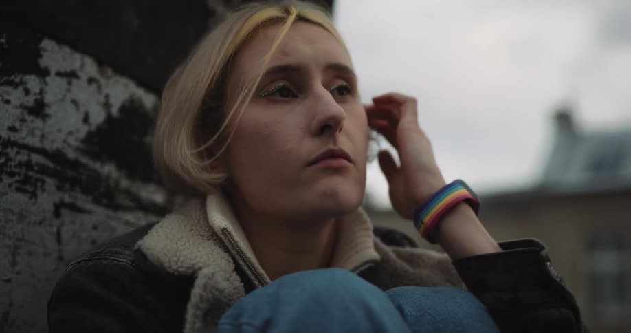 Sad blonde short haired woman sitting on the roof of a building at evening
