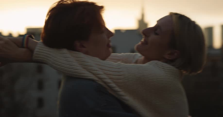 A couple is shown on a rooftop overlooking the city and they embrace and kiss