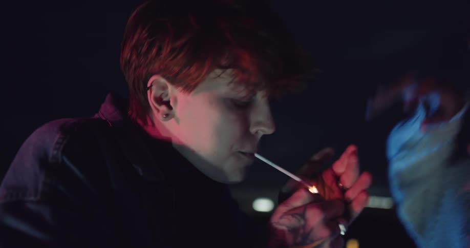A woman dances on a rooftop as another woman lights a cigarette for her and then they both dance and smoke