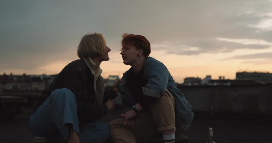 A couple kiss while sitting on their rooftop and drinking beer