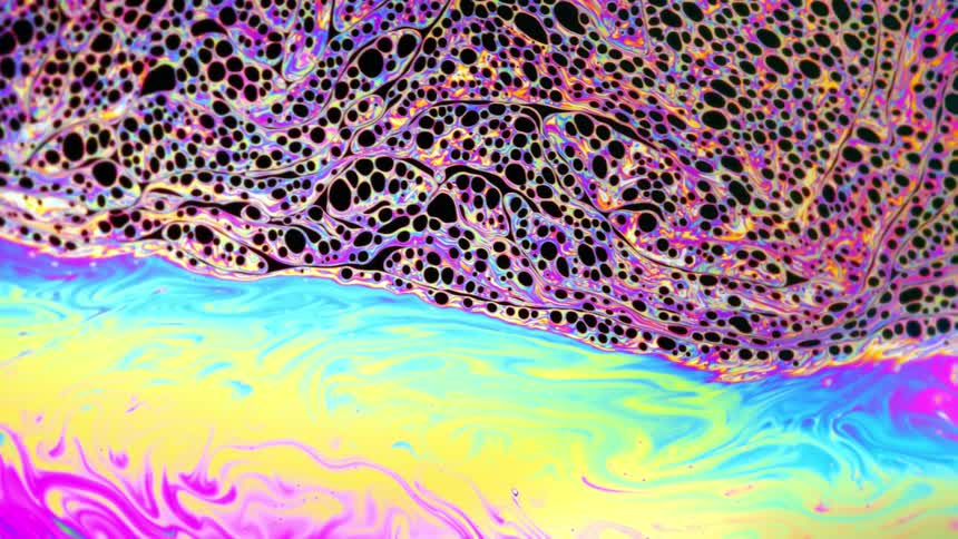 Layer of bubbles trapped on a colorful stream of liquid ink flowing over waves of bright multicolored swirls