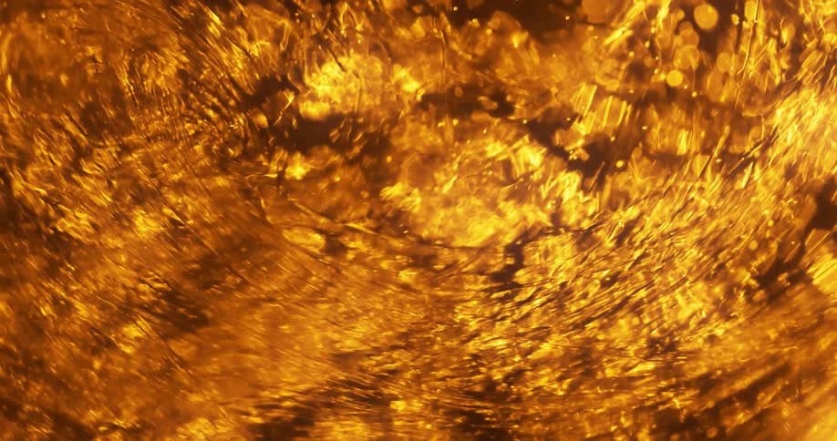 Golden spots flow in a rush under a transparent reflective lined surface causing mixture to swirl