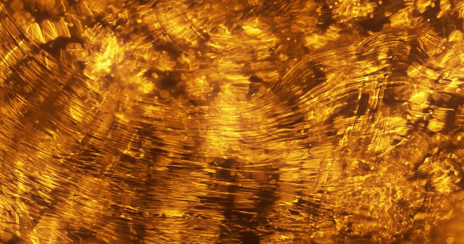 An oily film moves across water that is reflecting gold light