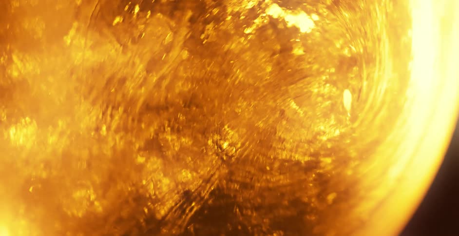 A viscous liquid swirls around as its mixed while illuminated with an amber light