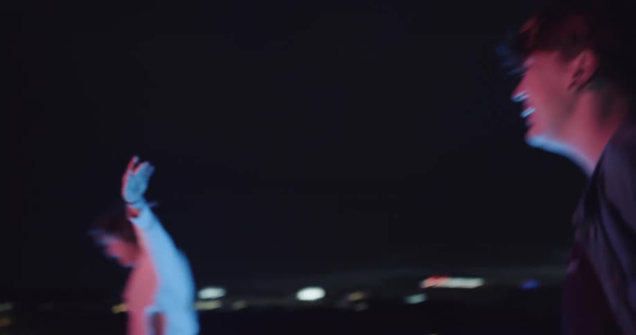 Two friends dancing outside on a rooftop with a bottle of booze at night