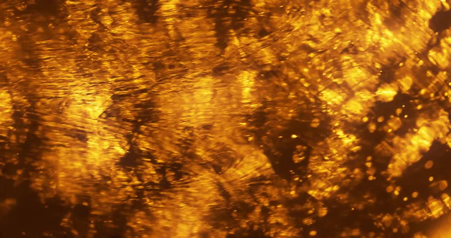 Gold warm yellow lights reflecting over the surface of a flowing liquid