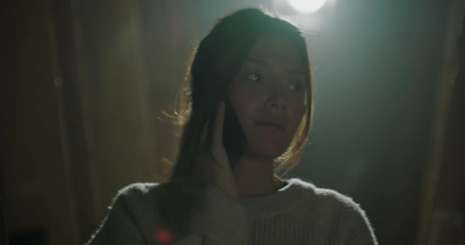 Woman with ponytail and beige sweatshirt talks on mobile phone in the attic