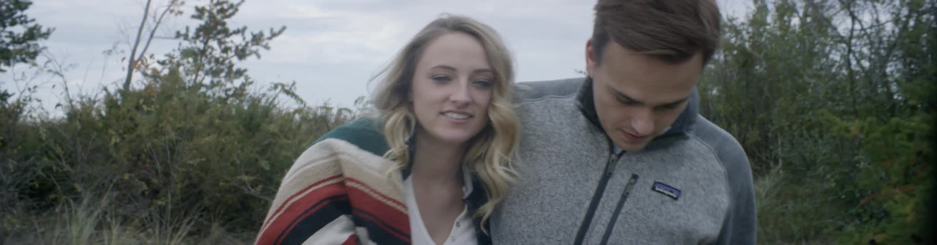 A man kisses a woman on her forehead as they walk on a beach