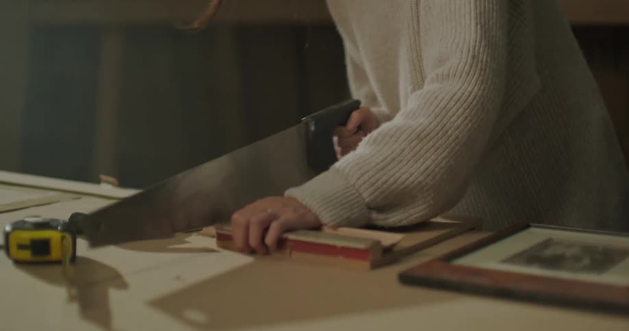 A female is sawing wood in a garage