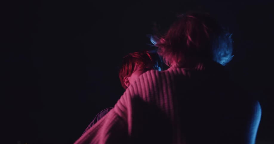 Neon lights flash as a man and woman dance on top of a rooftop