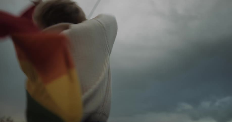 A woman dances and spins while waving a rainbow flag before jumping on her companions back