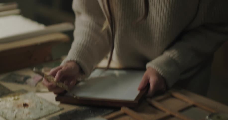 Woman applies colored paste to picture frame while working at table in workshop