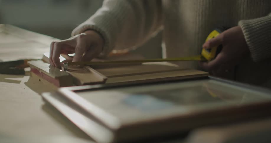 A woman holds a tape measure to measure a picture frame