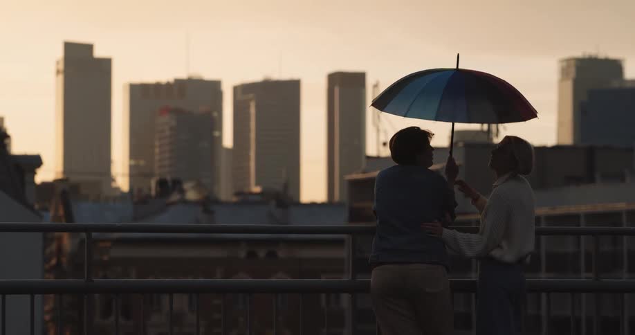 Young couple under a colorful umbrella on the roof of a building at evening